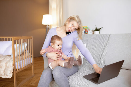 Stressed working young mother with little baby on her lap having business conversation on mobile phone, looking at laptop screen, home interior, copy space. Working mothers concept