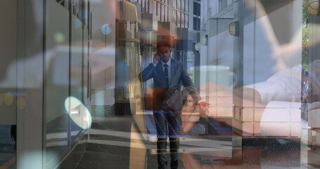 Walking suited professional speaking on smartphone in office corridor, with laptop typing overlay