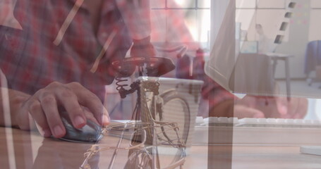 Operating man's hands moving mouse and typing on keyboard at office desk, with bicycle, coffee mug