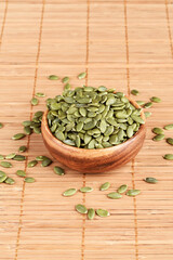 Peeled pumpkin seeds in a wooden bowl and on a mat.