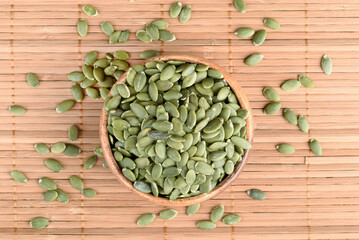 Top view of peeled pumpkin seeds in wooden bowl and on mat.
