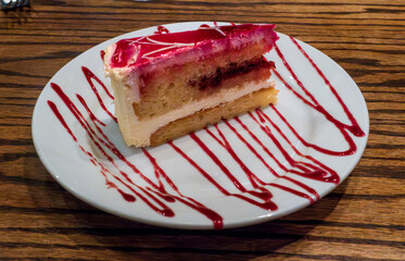 A slice of moist Limoncello cake is drizzled with vibrant raspberry sauce, blending zesty citrus and sweet berry flavors for a refreshing, elegant dessert experience.