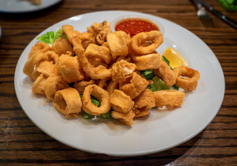 A white plate of golden fried calamari is served with zesty lemon slices and a side of rich marinara sauce, offering a crispy, tangy, and flavorful appetizer perfect for sharing.