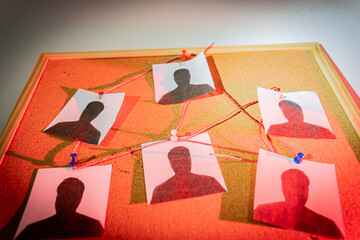Criminal investigation board with suspect photos connected by red thread on cork background
