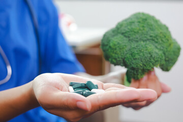 Nutritionist holding medicine and green vegetables to compare the choice of eating healthy foods instead of taking supplements. Dietitian. Medical Nutrition.