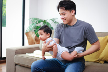 Asian father holding little baby playing rocking back and forth he smiles happily. The bond between...