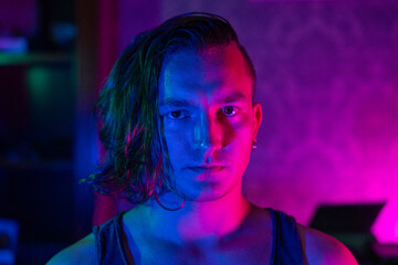 A young caucasian male with long hair and earrings is captured in moody neon lighting, highlighting contemporary urban style. vibrant pink and blue tones create a dramatic effect.