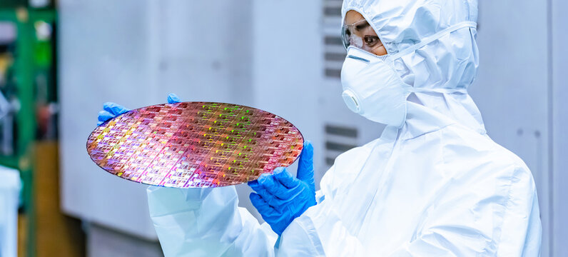 A female worker in protective clothing inspects silicon wafers in a semiconductor factory