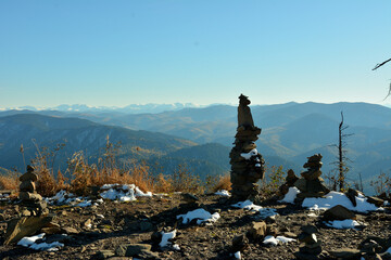 High pyramids of stones and dry grass sprinkled with first snow on the top of a cliff with a view of mountain ranges on a sunny autumn day.