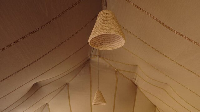Beige tent interior with handmade wicker lamps hanging from the ceiling. Rustic ceiling lights inside the tent. North African, desert style, interior decor.