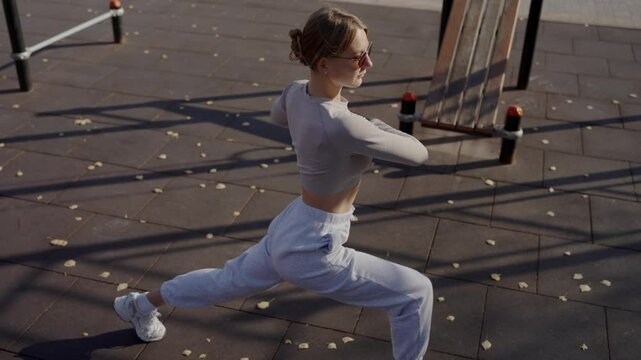 A young woman in stylish sportswear performs a dynamic stretch during an outdoor workout. Autumn leaves and urban setting add to the scene. Fitness Enthusiast Engaging in Dynamic Outdoor Exercise