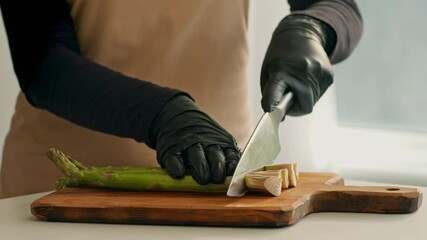 A chef in gloves skillfully cuts fresh asparagus on a wooden chopping board. The kitchen is bright and eco-friendly, emphasizing healthy cooking practices. Attention to detail is evident.