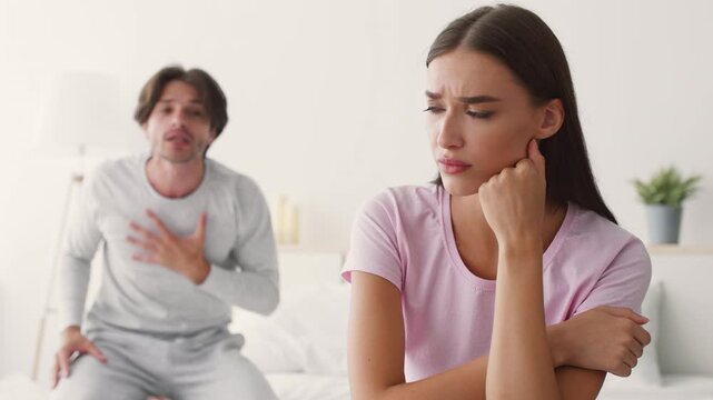 A man expresses frustration while a woman shows signs of distress, sitting on a couch in a modern living room setting. Their tense interaction reflects a deeper relationship issue.