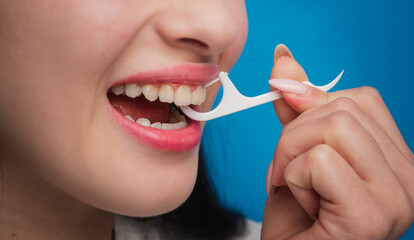 Close-up view of a woman flossing her teeth with a dental pick against a blue background.