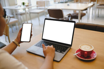 A person multitasking with a laptop and a smartphone, both with blank white screens. Ideal...