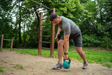 Man working out outdoors in the park, back exercise with kettle bell 