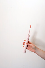 Hand holding a pink electric toothbrush against a plain white background, showcasing a minimal and modern hygiene product