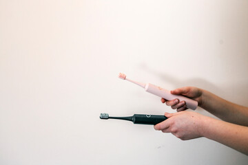 Hand holding a pink electric toothbrush against a plain white background, showcasing a minimal and...