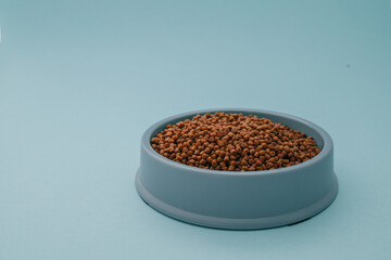Dry pet food spilled from a blue bowl on a light blue background. Minimalist concept for pet care and feeding