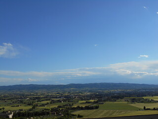 Fototapeta premium イタリア・アッシジの田園風景と遠くに続く山並み｜青空と広大な大地が広がる美しい風景 Scenic countryside view of Assisi, Italy｜Wide open fields and distant hills under a clear blue sky