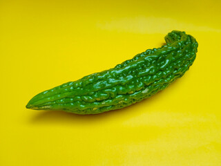 Fresh green bitter gourd or bitter melon isolated on yellow background.