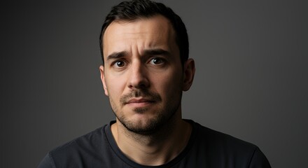 Fototapeta premium Portrait of a pensive man with a thoughtful expression, studio shot against a dark grey background