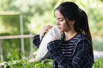 Asian teenage girl holding large sack over shoulder while standing in garden, participating in organic agriculture training and demonstrating responsibility and effort in outdoor learning