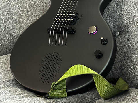 A sleek black Enya Nova Go Sonic electric guitar rests against a textured grey background, its vibrant green strap casually draped across the body.