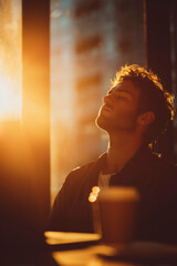 Man bathed in warm sunlight, eyes closed, peaceful moment, curly hair, glowing skin, golden hour serene