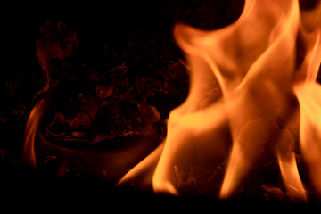 Close-up image of bright orange flames against a backdrop of black ash and burnt debris. A strong...