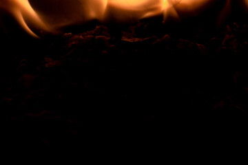 Close-up image of bright orange flames against a backdrop of black ash and burnt debris. A strong visual composition depicting the power, energy, and beauty of nature in the form of the fire element. 