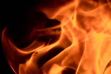 Close-up image of bright orange flames against a backdrop of black ash and burnt debris. A strong visual composition depicting the power, energy, and beauty of nature in the form of the fire element. 