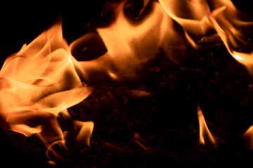 Close-up image of bright orange flames against a backdrop of black ash and burnt debris. A strong visual composition depicting the power, energy, and beauty of nature in the form of the fire element. 