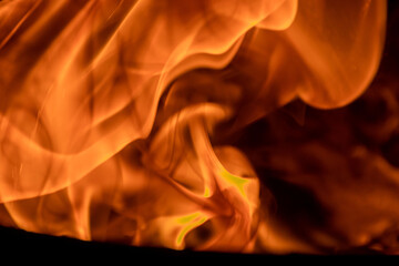 Close-up image of bright orange flames against a backdrop of black ash and burnt debris. A strong visual composition depicting the power, energy, and beauty of nature in the form of the fire element. 