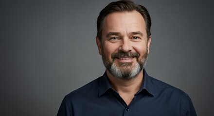 Portrait of a smiling middle-aged man with a beard, wearing a dark blue shirt against a gray background.