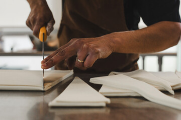 Close-up of a baker’s hands carefully rolling croissant dough on a metal countertop. The person is wearing a brown apron and has flour on their fingers, creating an authentic, artisanal atmosphere in 