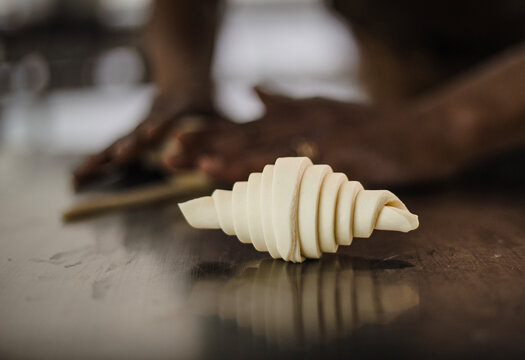 Close-up of a baker’s hands rolling croissant dough on a metal surface. Only the hands are visible, dusted with flour, emphasizing the artisanal baking process.