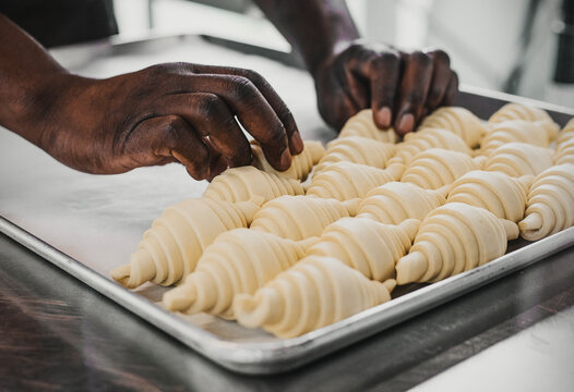 Close-up of a baker’s hands rolling croissant dough on a metal surface. Only the hands are visible, dusted with flour, emphasizing the artisanal baking process. - Powered by Adobe