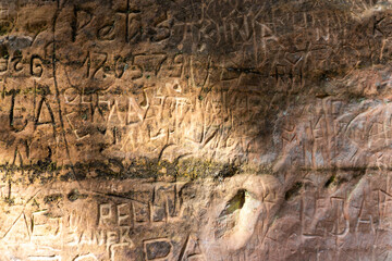Close-up of an ancient sandstone wall covered in engraved names and carvings, showcasing human...