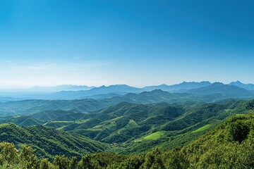 Obraz premium Panoramic mountain range view. Lush green hills stretch across a vast landscape under a clear blue sky
