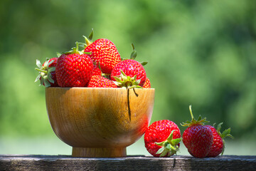 Fresh strawberries overflowing a wooden bowl on a sunny day