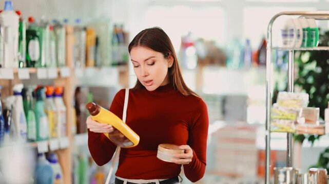 Woman in a household store chooses cleaning products for wooden surfaces. European woman looking at natural wood parquet care kit, she holds gels and paste