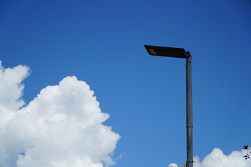 Modern streetlight against a vibrant blue sky dotted with fluffy white clouds.
