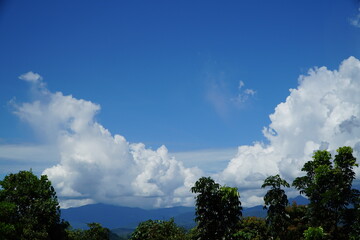 Vast expanse of a clear blue sky, dotted with fluffy white clouds, over a lush green mountain range.