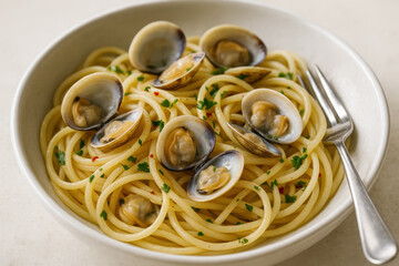 Spaghetti with fresh clams garnished with parsley and chili flakes served in a white bowl with a fork on a light background