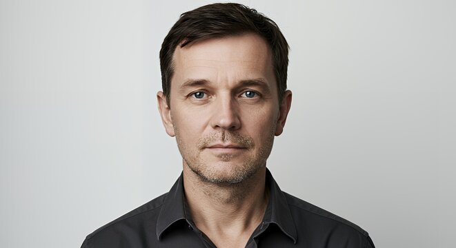 Portrait of a man with short brown hair, wearing a dark gray shirt, against a neutral background. Serious expression.