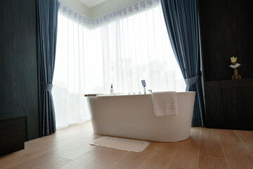 a white bathtub near a window with curtain