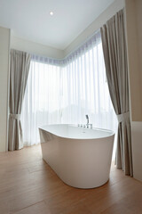 a white bathtub near a window with curtain