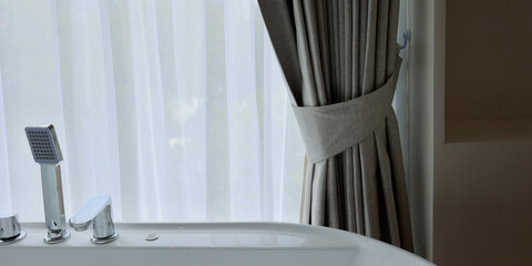 tap of bathtub near a window with curtain