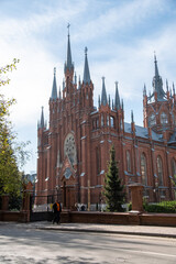 Gothic Revival church featuring multiple spires and intricate brick facade. The structure is surrounded by trees, adding to the majestic and historical ambiance of the scene.